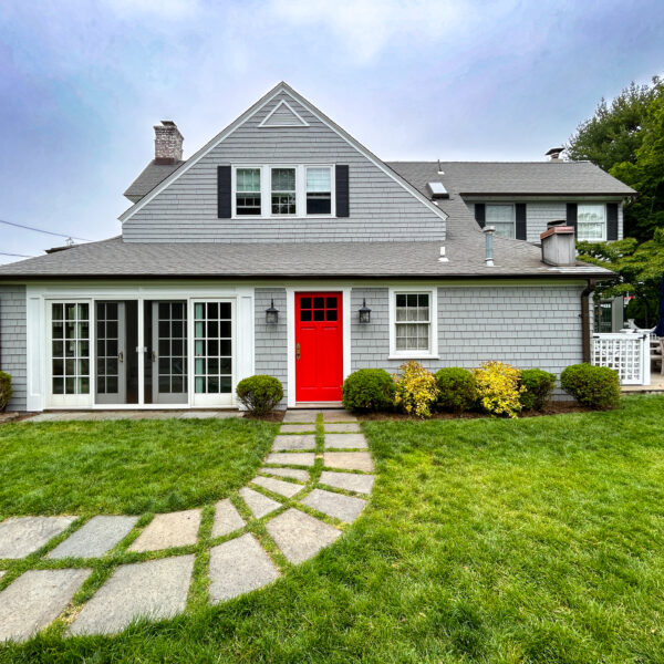 Gray clapboard house with a red front door, black shutters, white French doors and a curved stone path in the lawn