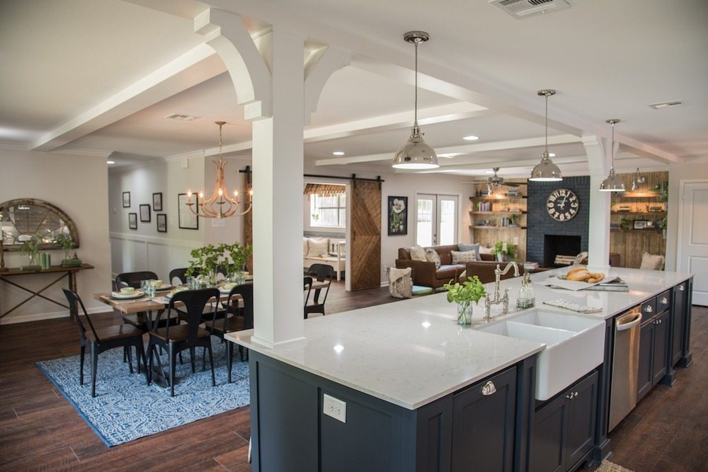Open-plan kitchen with a dark blue island, white countertop and farmhouse sink, open to a dining area and living room